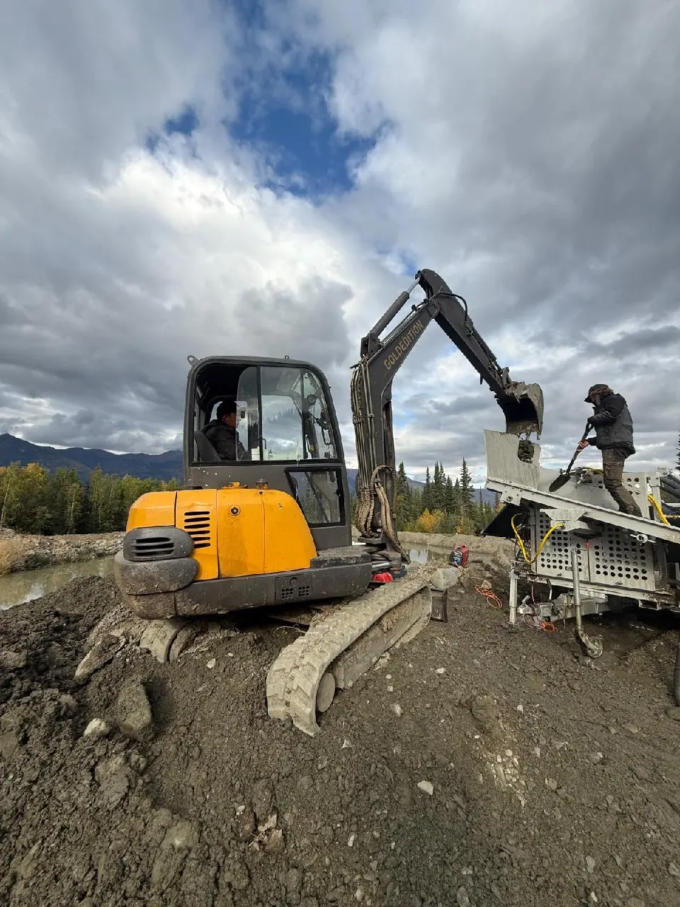 Mini excavator feeding a wash plant beside a creek
